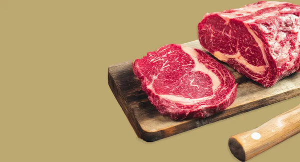 Whole ribeye joint with a ribeye steak cut from it on a wooden board – cut your own steaks