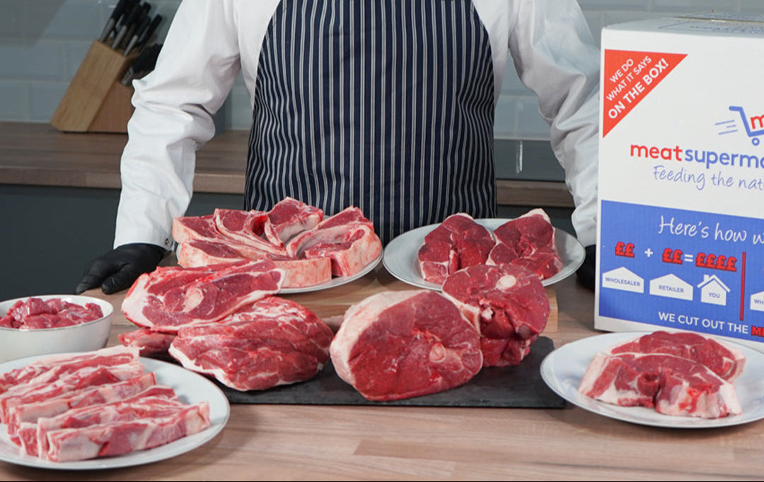 Butcher behind a counter with raw lamb leg steaks, beef joints and steaks beside a meatsupermarket.com delivery box