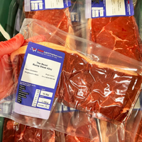 Packaged rump steak with a label held by a gloved hand.