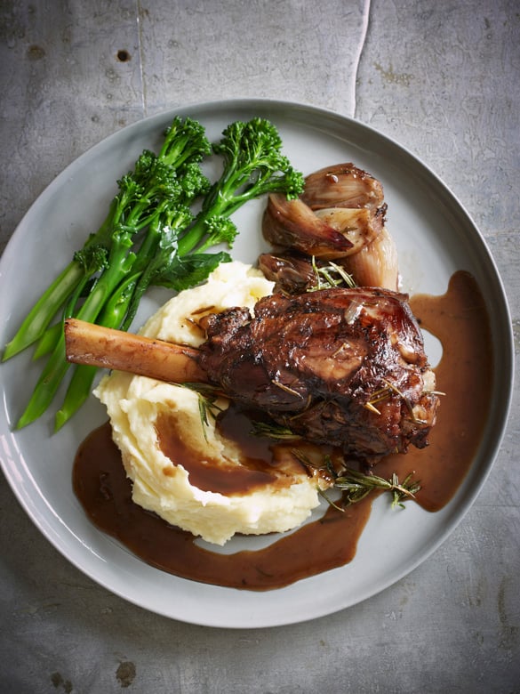 Two raw lamb shanks with rosemary on a white plate – slow-cook lamb from our online butcher